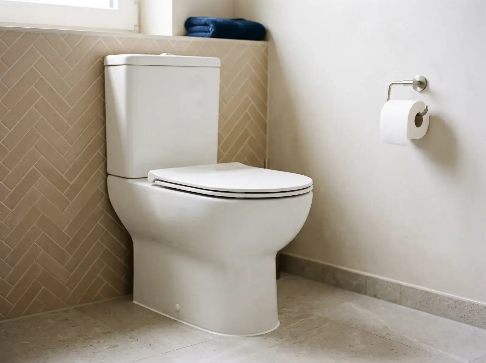 WC neuf en céramique blanche au sol, avec réservoir, posé devant un carrelage beige en chevrons